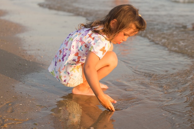 Das kleine süße Mädchen sitzt und spielt am Strand