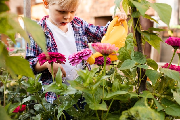 Das Kleinkind gießt Blumen im Garten mit einer Gießkanne