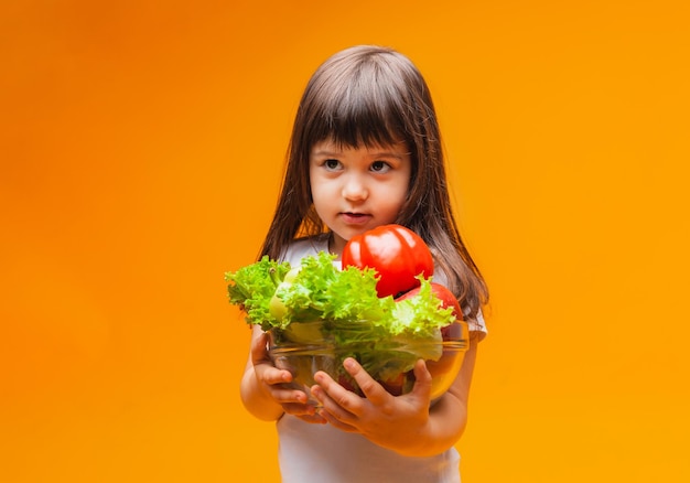 Das Konzept der Bio-Lebensmittel Kleines Mädchen, das einen Korb mit Obst und Gemüse auf gelbem Hintergrund hält Gesunde Babynahrung