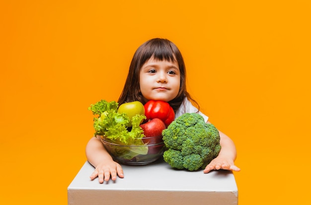 Das Konzept der Bio-Lebensmittel Kleines Mädchen, das einen Korb mit Obst und Gemüse auf gelbem Hintergrund hält Gesunde Babynahrung