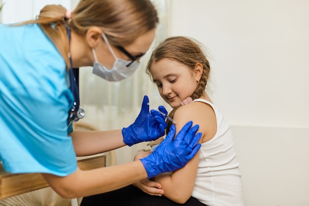 Das Konzept der Impfung. Ärztin, die niedliches kleines Mädchen in der Klinik impft