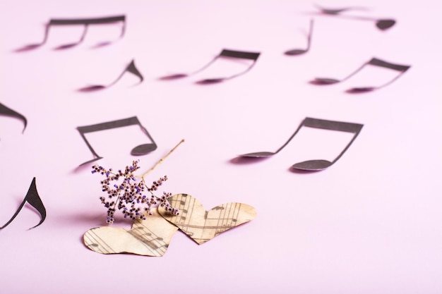 Foto das konzept der liebe zur musik zwei papierherzen trockene blumen und noten auf einem rosa hintergrund