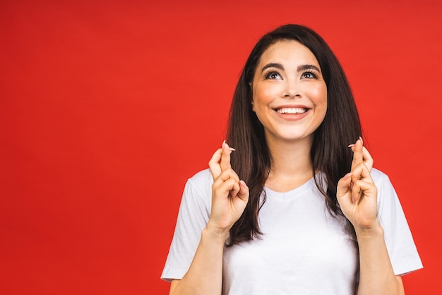 Das Konzept der Meditation Eine schöne junge Frau steht in einer meditativen Pose und genießt eine ruhige Atmosphäre, die ihre Hände in einer Gebetsgeste isoliert auf rotem Hintergrund hält