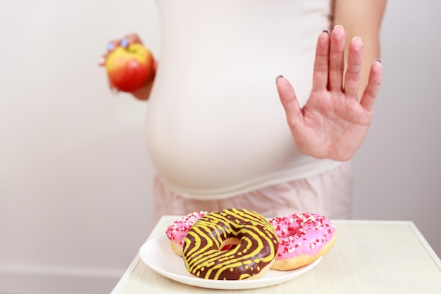 Das Konzept der richtigen Schwangerschaftsernährung schwangere Frau mit Donuts und Apfel