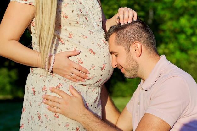 Das Konzept der Schwangerschaft, die schwangeres Paar im Park wartet, Nahaufnahme Mann, der den schwangeren Bauch seiner Frau mit Liebe in Erwartung des Neugeborenen umarmt