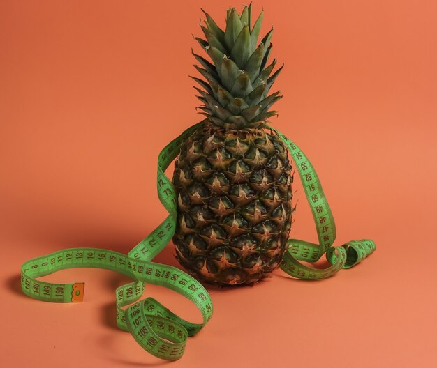 Das Konzept des Abnehmens. Fruchtdiät. Ananas eingewickelt in ein Maßband auf orangefarbenem Hintergrund