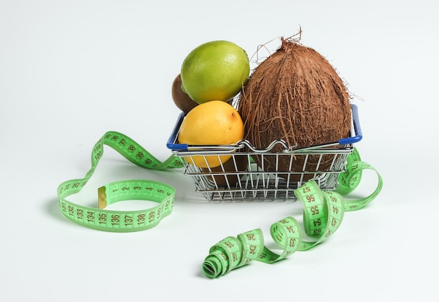 Das Konzept des Abnehmens. Tropische Früchte und Maßband im Einkaufskorb auf weißem Hintergrund. Gesundes Essen. Fruchtdiät. Draufsicht