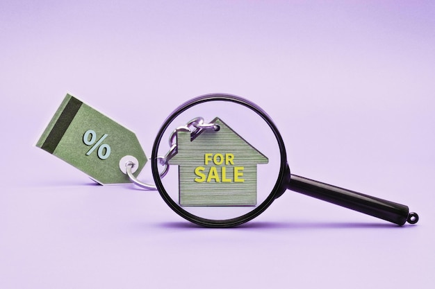 Das Konzept des Verkaufs von Hypotheken und Mieten von Wohnungen und Immobilien Hausverkauf Schlüsselanhänger in Form eines Hauses mit einem Schlüssel unter einer Lupe Kopieren Sie Platz