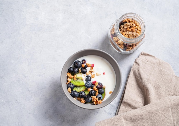 Das Konzept eines gesunden Frühstücks mit vegetarischem Joghurt-Müsli und frischem Obst, Kiwi und Heidelbeeren auf blauem Hintergrund Draufsicht und Kopie xAspace