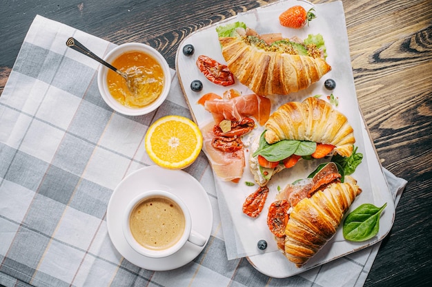 Das Konzept eines herzhaften und leckeren Frühstücks aus frischen klassischen Croissants mit verschiedenen Toppings aus Ricotta-Jamón-Avocado-Erdbeeren, sonnengetrockneten Tomaten und französischem Senf