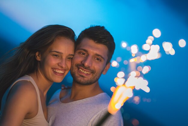 Das Lächelnpaar hält einen Feuerwerksstock. abend nacht zeit