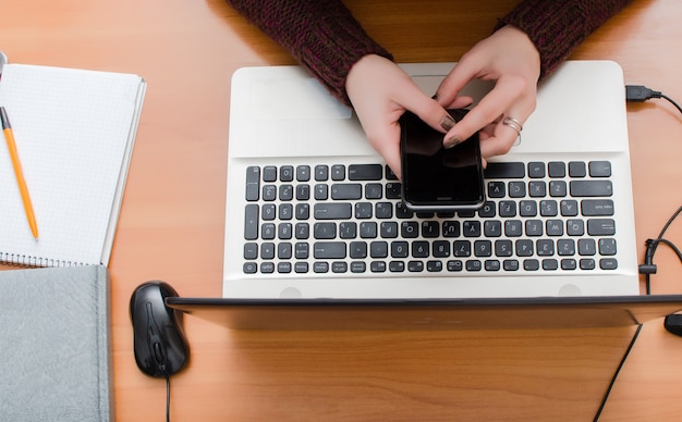 Das Mädchen arbeitet am Computer und hält ein Mobiltelefon in der Hand