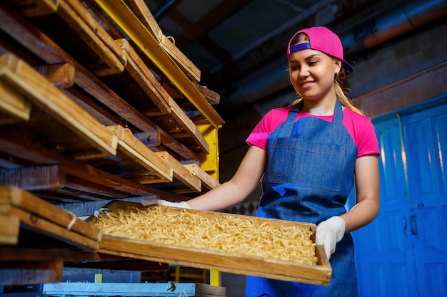 Das Mädchen arbeitet an der Herstellung von Spaghetti. Nudeln machen. Teigwarenfabrik. Bühnenproduktion von Nudeln. Rohe Nudeln. Arbeiter mit einer Schachtel Nudeln.