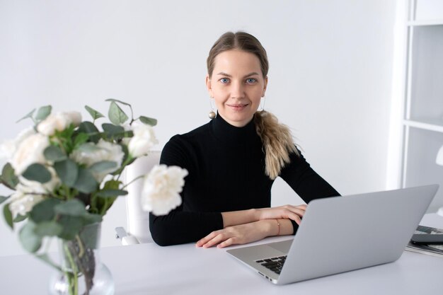 Das Mädchen arbeitet in einem weißen Büro mit einem Laptop und Blumen auf dem Tisch