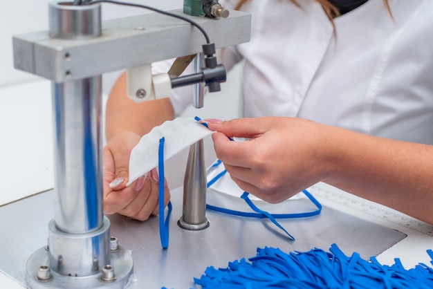 Das Mädchen arbeitet in einer Fabrik für die Herstellung von medizinischen Masken mit Nanofaser und Lötschleifen mit Ultraschall auf einer Maschine.