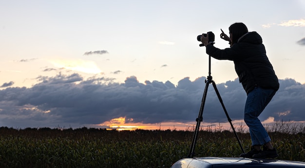 Das Mädchen auf dem Dach des Autos fotografiert den Sonnenuntergang mit einem Stativ.