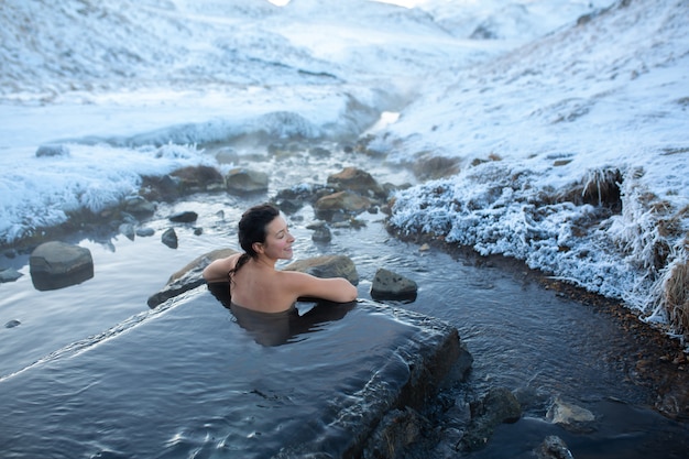 Das Mädchen badet in einer heißen Quelle unter freiem Himmel mit herrlichem Blick auf die schneebedeckten Berge. Unglaubliches Island im Winter