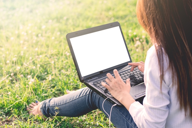 Das Mädchen benutzt einen Laptop auf einem grünen Gebiet mit einem Morgensonnenschein