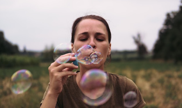Das Mädchen bläst Seifenblasen Eine junge Frau sitzt in der Natur und bläst Seifenblasen Das Gesicht vor