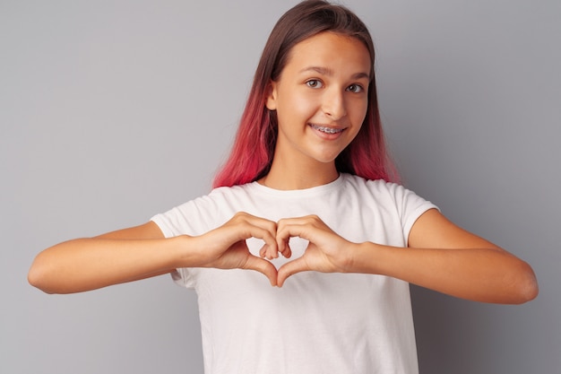 Das Mädchen des jungen jugendlich, das ihr Herz mit ihren Händen berührt, überreicht grauen Hintergrund