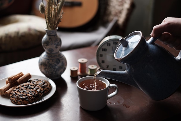 Das Mädchen gießt den Tee in eine Tasse Frühstück in gemütlicher Atmosphäre zu Hause