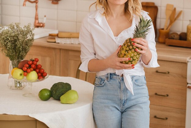 Das Mädchen hält eine Ananas vor sich in der Küche des Hauses Obst und Gemüse auf dem Tisch liegen