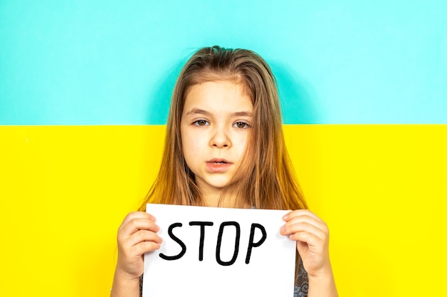 Foto das mädchen hält gegen den hintergrund der ukrainischen flagge ein stoppplakat in den händen