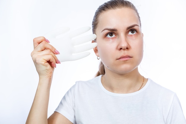 Das Mädchen hält weiße medizinische Handschuhe in den Händen. Schutz vor Keimen und Viren. Sie trägt ein weißes T-Shirt auf weißem Hintergrund.