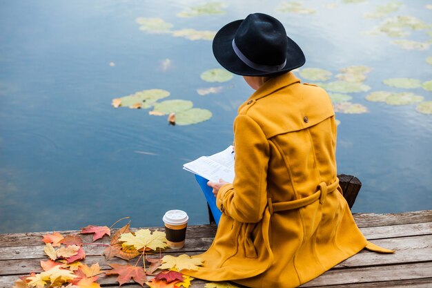 Das Mädchen im Herbst sitzt am Wasser. Herbst. Blätter. Gelb Rot. Kaffee