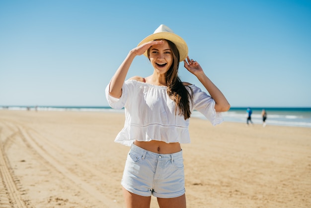 Das Mädchen im Hut mit den Haaren sieht freudig jemanden am Strand an. Erkennungsemotion