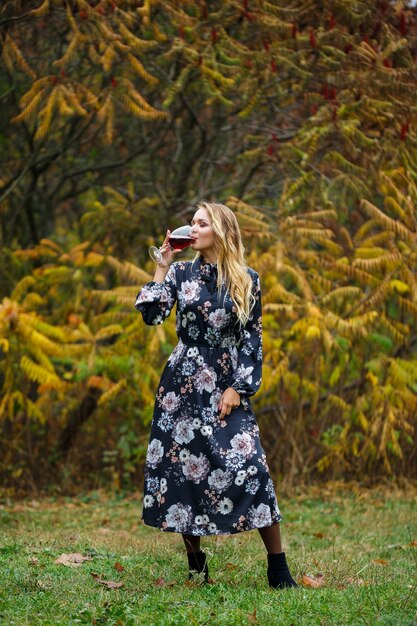 Das Mädchen im Kleid hält ein Glas Rotwein im Herbstwald