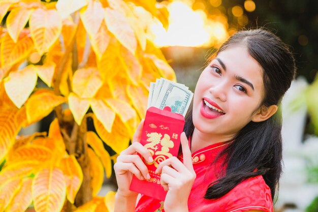 Das Mädchen im roten Kleid chinesischer Abstammung ist mit dem roten Umschlag mit dem Dollar glücklich.