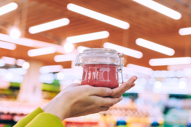 Das Mädchen im Supermarkt hält ein Glas Honig in der Hand. vor dem Hintergrund von Lampen.