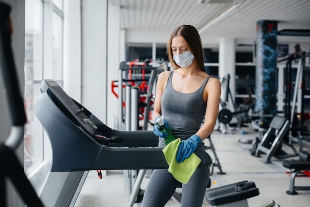 Das Mädchen in der Maske desinfiziert die Fitnessgeräte während einer Pandemie.