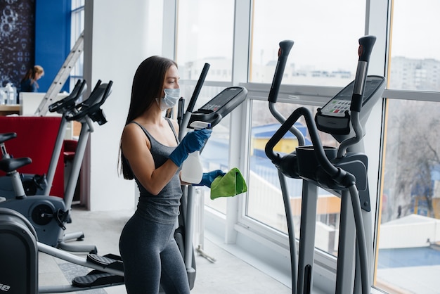 Das Mädchen in der Maske desinfiziert die Fitnessgeräte während einer Pandemie.