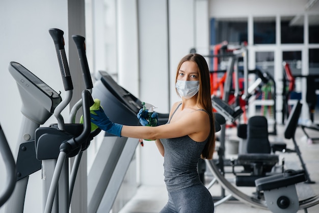 Das Mädchen in der Maske desinfiziert die Fitnessgeräte während einer Pandemie.