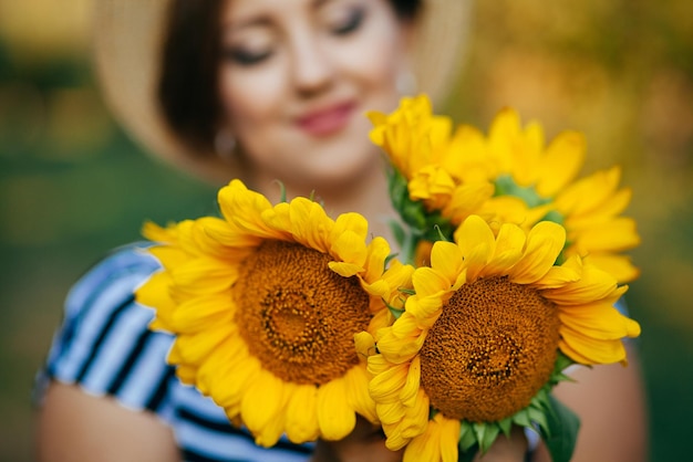 Das Mädchen in einem Hut mit einem Strauß Sonnenblumen posiert