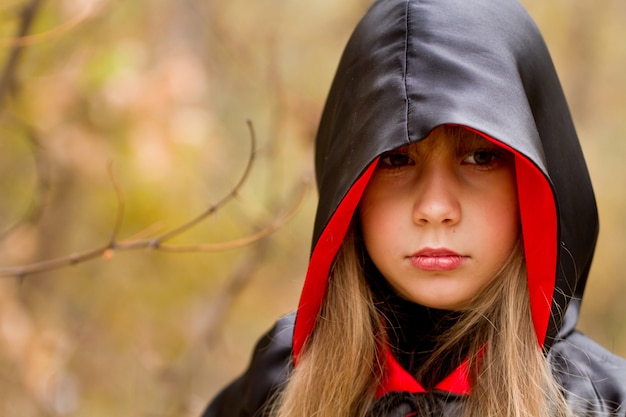 Das Mädchen in einem roten und schwarzen Umhang im Wald