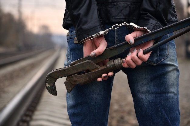 Das Mädchen in Handschellen mit dem Rohrschlüssel auf der Eisenbahnlinie