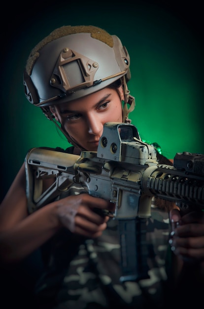 Das Mädchen in militärischer Spezialkleidung posiert mit einer Waffe in den Händen auf dunklem Hintergrund im Dunst