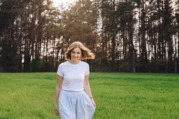 Das Mädchen ist blond, braunes Haar, trägt ein weißes Hemd und einen blauen Midirock. Auf dem Feld durch das grüne Gras gehen. Porträt eines Mädchens. Positiv und lächeln.