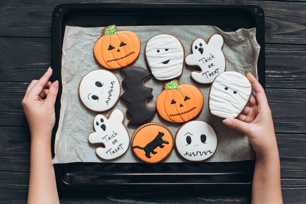 Das Mädchen kochte Lebkuchen für Halloween und hielt das Netz mit Pergament auf einem schwarzen hölzernen Hintergrund.