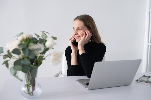 Das Mädchen lacht und telefoniert im Büro neben ihrem Laptop