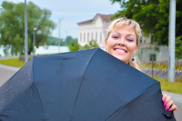 Foto das mädchen lächelt glücklich und versteckt sich hinter einem regenschirm