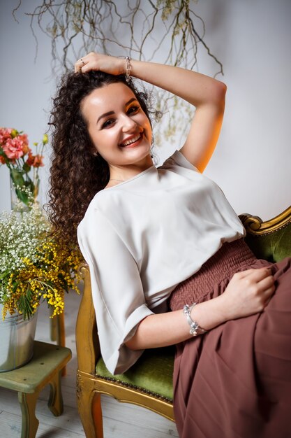 Das Mädchen lächelt in einem braunen Rock sitzt auf der Couch. herum sind frische Blumen in einer Vase.