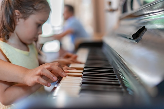 Das mädchen lernt klavier spielen, hört aufmerksam den anweisungen des lehrers zu, drückt die tasten und versucht, die melodie zu wiederholen und auswendig zu lernen.