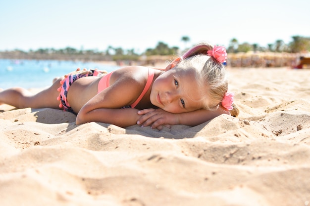 Das Mädchen liegt auf dem Strandsand in der Nähe des Meeres und nimmt ein Sonnenbad