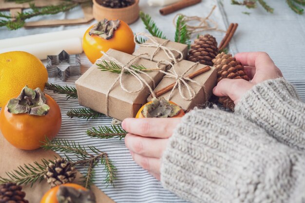 Das Mädchen macht eine Neujahrskomposition von Geschenken Verpackt mit ihren eigenen Händen in Kraftpapier, Draufsicht, Nahaufnahme. Frohe Weihnachten-Hintergrund. Vorbereitung auf den Urlaub. Weihnachtskonzept.