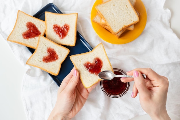 Das Mädchen macht einen Toast, auf dem das Herz aus Marmelade besteht Überraschendes Frühstückskonzept im Bett Romantik zum Valentinstag