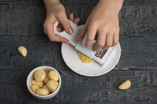 Das Mädchen mahlt frischen Knoblauch mit einer speziellen Reibe. Ein beliebtes Gewürz für die Küche.